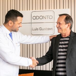 Dr. Luis Gustavo shaking hands with a patient, showcasing a friendly and welcoming interaction in a dental clinic.