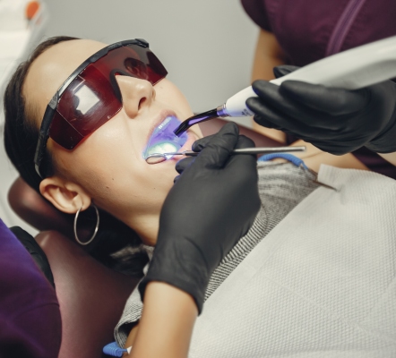 A female patient on dental chair getting teeth whitening treatment by a dentist