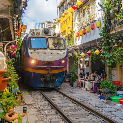 Train passing through Hanoi Train Street in Vietnam with few tourists taking pictures