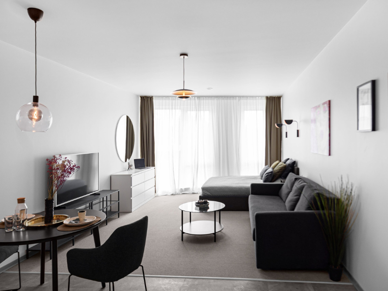 Cozy bedroom in a Lithuania post-surgery stay, featuring a black bed, sofa, chair, and closed window blinds for restful recovery.